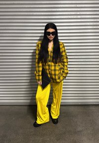 Oversized yellow plaid blazer teamed with vibrant yellow wide-leg trousers. A black clutch and platform boots finish off the outfit. Dark sunglasses are worn.