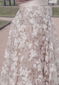 Doorzichtig, beige rokje met witte bloeiende kant overlay. Plissé ontwerp, gladde textuur en een zachte tailleband, wat zorgt voor een vloeiende silhouet.