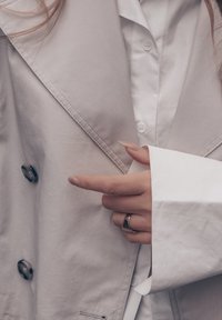 Heleroheline väliskate suure krae, nööpidega kinnituse ja tekstuurse kangaga. Selle all on nähtav valge nööbitav särk. Käel hõbedane sõrmus.