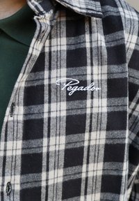 Zwart-wit geblokt flanellen shirt met een zachte textuur en een witte geborduurde "Pegador" logo op de voorkant. Kraag en knoopsluiting ontwerp.