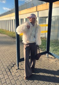 Include o jachetă albă pufoasă, hanorac ușor, pantaloni maro cu picioare largi și o șapcă roz. Accesoriile includ o geantă maro circulară.