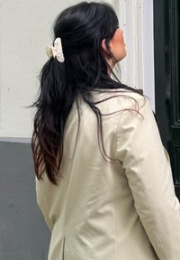 Light beige blazer with a smooth texture, worn over long dark hair styled with a cream-coloured hair clip featuring floral accents.