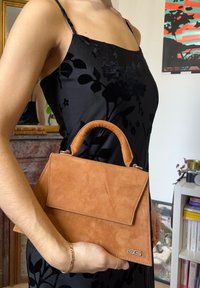 Pruun samet-nahast käekott, millel on struktureeritud kuju ja ümar ülemine käepide. Omab klapiga sulgemist ja hõbedast logo aktsenti.