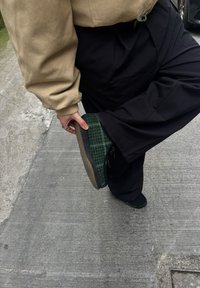 Zöld és fekete kockás papucs texturált felülettel és barna gumitalppal, egy betonfelülettől felemelt lábon viselve.