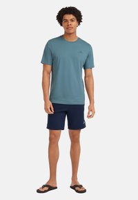 Men's teal cotton t-shirt, short sleeves, round neck; matched with navy shorts and black flip-flops. Simple logo on the t-shirt.