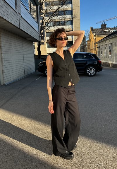 Chaleco negro de rayas con un diseño ajustado y cierre de botones, combinado con pantalones holgados negros y calzado negro robusto.