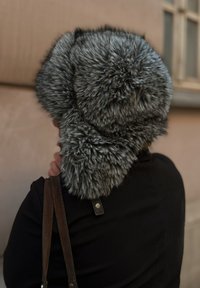 Fuskepelslue i grå, med en rund form og tykk, myk tekstur. Passer tett med en lærreimdetalj på en svart jakke.