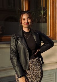 Chaqueta de motorista de cuero negro sobre una blusa negra de canalé, combinada con una falda beige con estampado de leopardo. La luz solar natural resalta la textura.