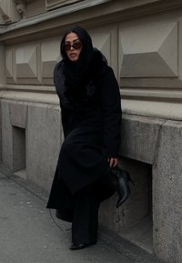 Fekete hosszú kabát műszőrme gallérral, fekete nadrággal és hegyes orrú magas sarkú cipővel párosítva. Sötét napszemüveget és hozzá illő fekete hidzsábot visel.