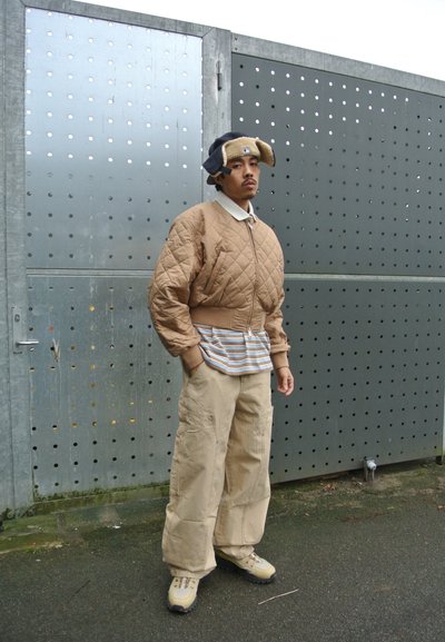 Chaqueta beige acolchada con puños acanalados, camiseta a rayas, pantalones cargo y zapatillas beige. Gorra con acentos en las orejas en azul marino y beige.