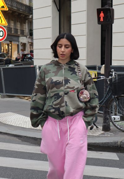 Sudadera con cremallera de camuflaje con un bolsillo frontal, combinada con pantalones de chándal rosas holgados. Accesorio incluye una pequeña bolsa redonda con cadena.