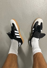 Zwart-witte sport schoenen met een rubberen zool, voorzien van drie witte strepen en een kenmerkend neusdesign, gedragen met witte sokken.