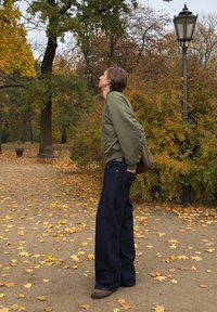 Roheline bomberjakk, tumedad laia säärega teksad, pruunid saapad. Väljas keskkond sügiseste lehtedega ja taustal laternapost.