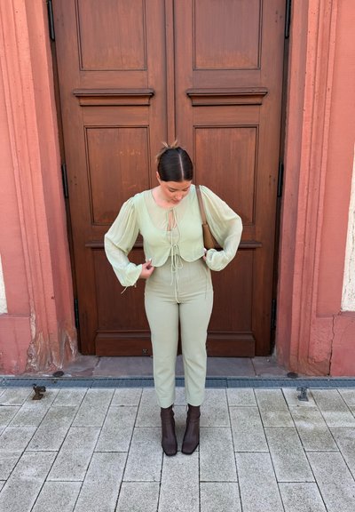 Top transparente verde claro con mangas abullonadas, cintura ceñida y detalle de lazo, combinado con pantalones ajustados a juego y botas de tobillo marrones.