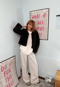 Personne en tenue décontractée et veste noire posant dans un coin avec des affiches motivantes et une boule disco au sol.