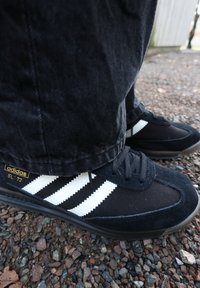 Baskets noires Adidas SL '72 avec rayures blanches, en toile et suède, surface texturée, semelles en caoutchouc et accents de logo dorés.