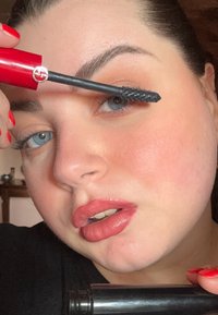 Musta ripsivärisivellin pidetään silmän yläpuolella, esittelee kiiltävän punaisen putkilon. Sileä iho, jossa on hienovarainen persikkapunastus ja nudehuulipuna. Kirkkaansiniset silmät.