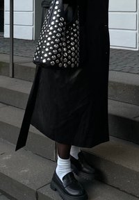 Μαύρη δερμάτινη τσάντα με ασημί καρφιά, μαύρο μακρύ παλτό, μαύρα χοντρά παπούτσια και άσπρες κάλτσες. Στεκόμενος σε γκρι πέτρινες σκάλες.