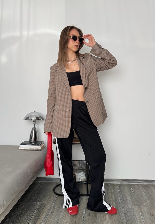 Rutete oversized blazer, svart crop top, svarte joggebukser med hvite striper, rød håndveske, og rødt fottøy. Solbriller fullfører looken.