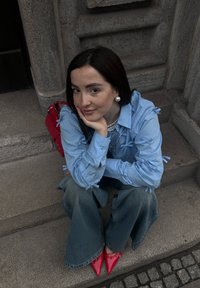 Chemise bleu clair avec des détails en nœud, jean denim évasé taille haute et escarpins rouges à bout pointu ; boucles d'oreilles en perles argentées et un sac à main rouge.