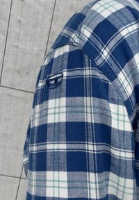 Chemise en flanelle à carreaux bleus et blancs avec manches courtes, dotée d'une poche à bouton et d'une texture lisse.