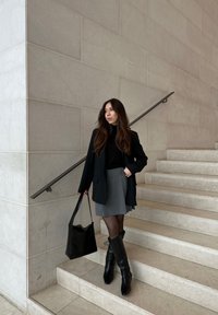 Μαύρο σακάκι πάνω από μαύρο τζέρσεϊ, γκρι πλισέ φούστα, μαύρες καλσόν και μαύρες μπότες με τακούνι μέχρι το γόνατο. Κρατάει μια μαύρη τσάντα ώμου.