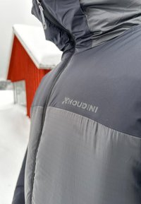 Houdini geïsoleerde jas met een twee-tone ontwerp met een donkergrauw bovenste gedeelte en lichtere grijze onderste panelen, een gladde textuur en een rits aan de voorkant.
