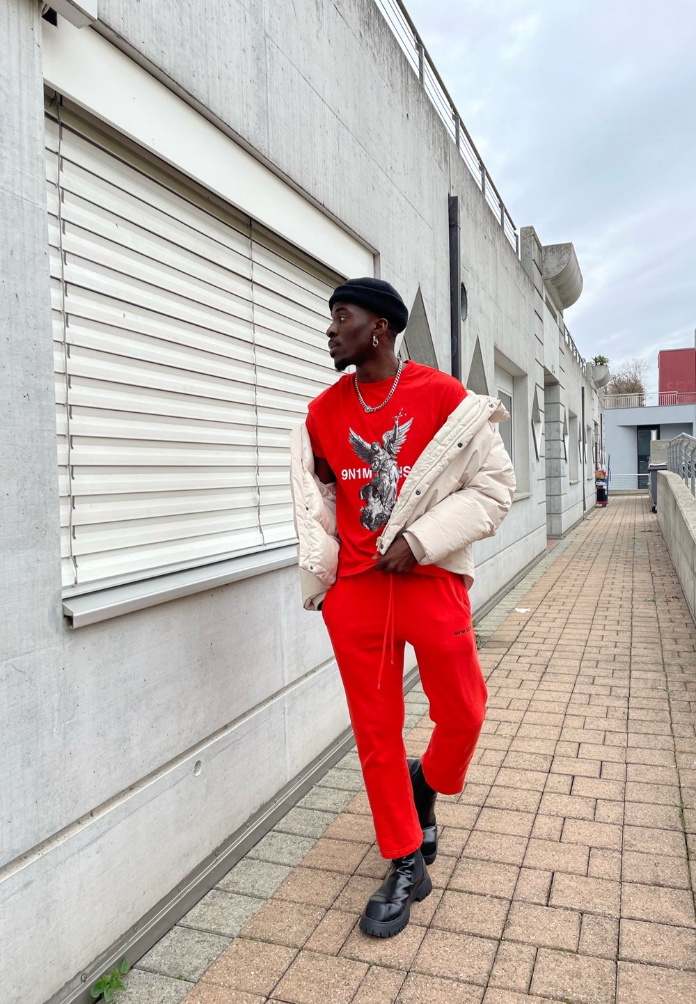 Red graphic t-shirt featuring an eagle design, paired with red sweatpants and a cream puffer jacket. Black boots complete the outfit.