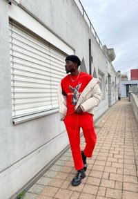 Red graphic t-shirt featuring an eagle design, paired with red sweatpants and a cream puffer jacket. Black boots complete the outfit.