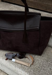 Mørkebrun lær- og suedetotekveske på steintrapper, med skilpaddemønstret solbriller og en beige Summer Fridays hudpleierør i nærheten.