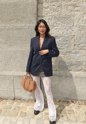 Blazer de rayas marinas, vestido mini gris, pantalones acampanados de encaje blanco y bolso marrón, con zapatos de plataforma negros. Fondo de piedra texturizada.