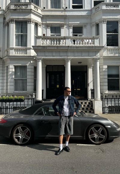 Coche deportivo gris con techo convertible negro; el edificio presenta columnas blancas, grandes ventanas y molduras decorativas en el fondo.