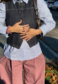 Vestă din denim peste o cămașă în dungi, cu pantaloni roz cu picioare largi. Accesoriile includ mai multe inele și un scrunchie roz pe încheietură.