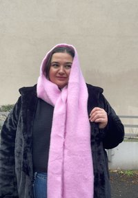 Lys lyserød uldscarf draperet over skuldrene, båret med en sort faux fur frakke. Begge genstande er bløde i teksturen med et simpelt design.