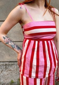 Rozā un sarkana svītrainā kleita ar kvadrātveida dekoltē, plānām plecu siksnām un savilkumu jostasvietā. Roka rotāta ar ziedu tetovējumu.