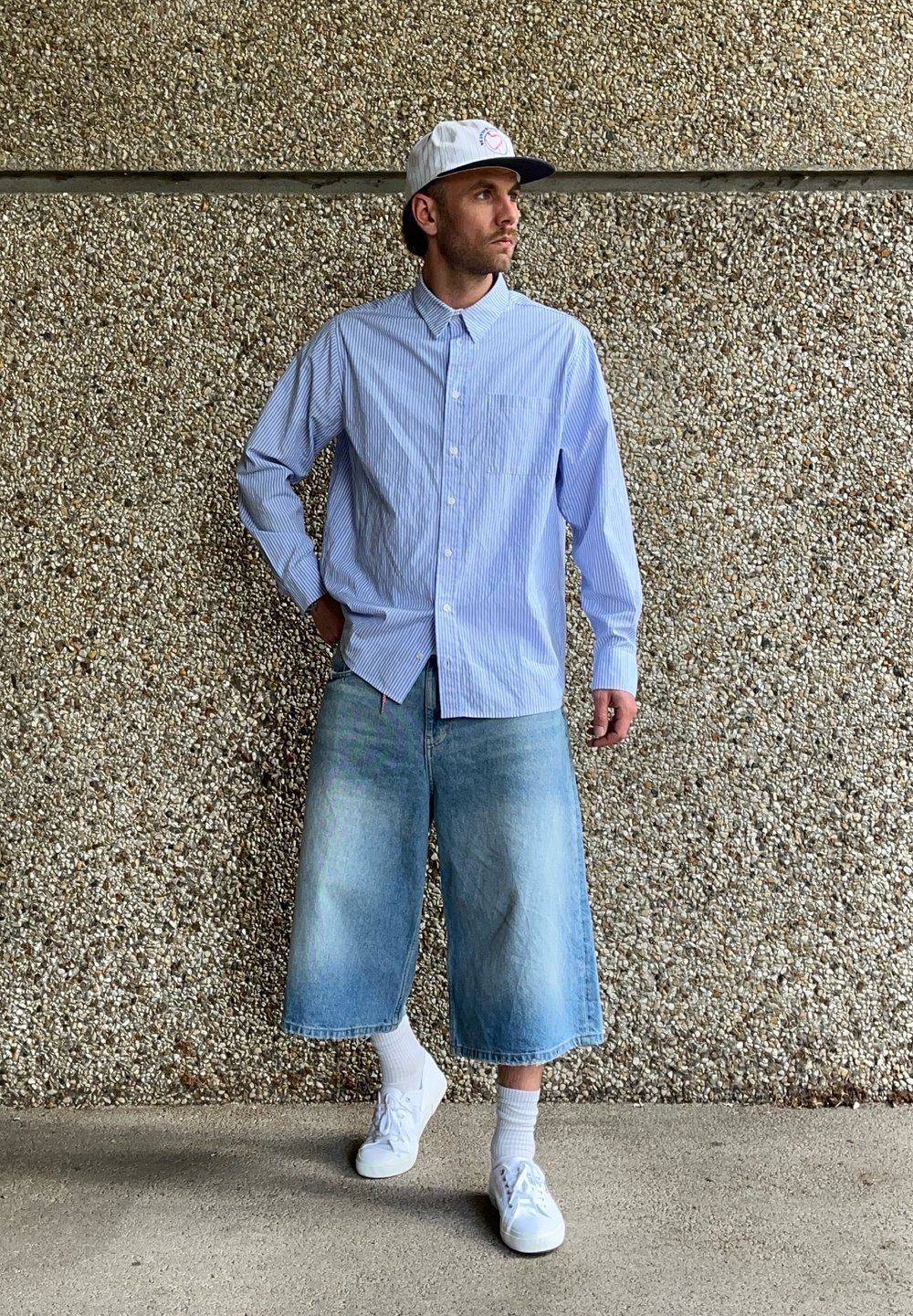 Vaaleansininen raidallinen pitkähihaisyntopali, farkku culottes, valkoiset tennarit ja valkoinen lippalakki logolla. Taustalla on teksturoidun betoniseinän.