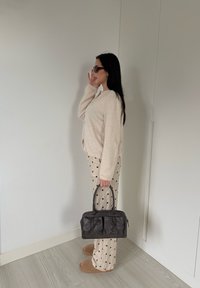 Cardigan beige en tricot, pantalon crème à pois, chaussons marron et sac en cuir noir avec deux poches avant. Mannequin portant des lunettes de soleil.