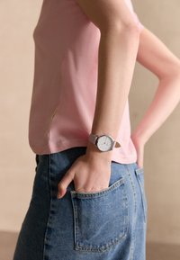 Roze katoenen t-shirt met korte mouwen, gecombineerd met een blauwe spijkerrok. Een zilveren horloge met een witte wijzerplaat en lavendelbandje is om de pols gedragen.