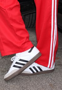 Hvite Adidas Samba-sko med tre svarte striper, grå gummisåle, kombinert med røde treningsbukser med hvite sidestriper.