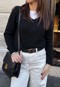 Sort v-hals sweater, hvid t-shirt under, parret med cremefarvede brede bukser. Sort bælte med guld YSL-logo. Sort skuldertaske.