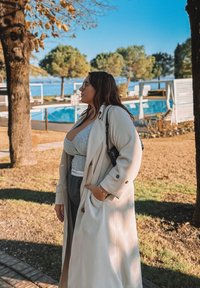 Um longo casaco bege sobre uma blusa cinza e calças de cintura alta, com uma mala preta. Apresenta botões oversized e um corte descontraído.