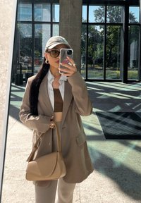 Μπεζ υπερμεγέθη σακάκι, λευκό πουκάμισο, καφέ cropped top, μπεζ τσάντα χειρός, ηλιακά γυαλιά και καπέλο. Μαλακές υφές, απλές γραμμές και ουδέτερη χρωματική παλέτα.