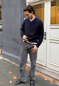 Tumesinine ribaga kudum, valge särgi peal, koos pleekinud hallide laiade pükstega ja mustade kingadega, seismas kõnniteel.