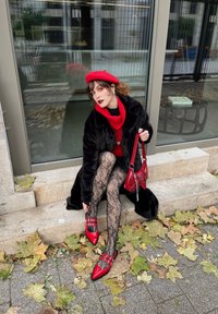 Rosso tacchi alti con cinturini, calze di pizzo nere, maglione rosso e cappotto nero. Seduta su gradini di pietra circondata da foglie autunnali.