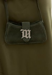 Grøn ruskinds håndtaske med et sølv "M" emblem, der har en flad rektangulær form, en kort skulderrem og syede detaljer langs kanterne.
