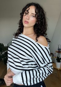 Črtasta jopica z črnimi in belimi horizontalnimi črtami, prevelik kroj, mehak material, off-shoulder zasnova in rebrasti manšeti.