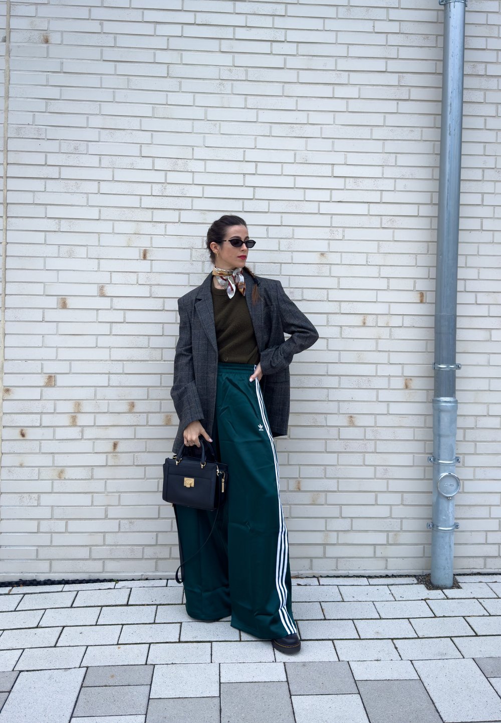 Oversized grå rutete blazer, olivengrønn topp, tealfargede vide bukser med hvite striper, liten svart veske, mønstret skjerf, svarte solbriller.