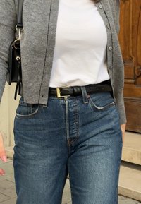 Γκρίζα ζακέτα πάνω από λευκό μπλουζάκι, σε συνδυασμό με ψηλόμεσα μπλε τζιν παντελόνια και μαύρη ζώνη με μεταλλική χρυσή πόρπη.