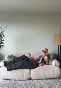 Crni i srebrni uzorak na kratkom topu i širokim tamnim hlačama koje nosi osoba koja se opušta na svijetloj, mekoj sofi s ukrasnim jastučićima.