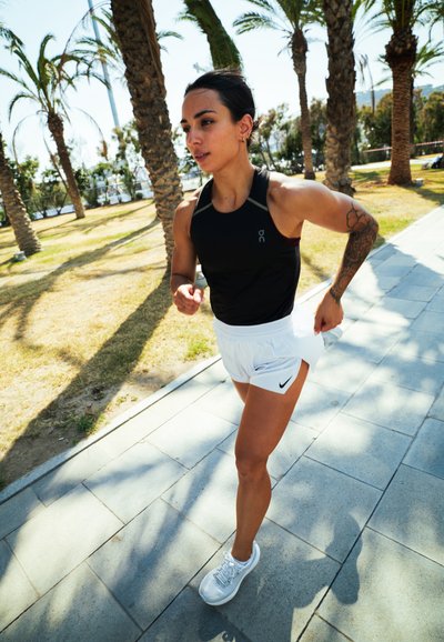 Ropa deportiva: camiseta sin mangas negra y pantalones cortos blancos con el logotipo negro de Nike. Zapatillas ligeras, corriendo por un camino de piedras entre palmeras.